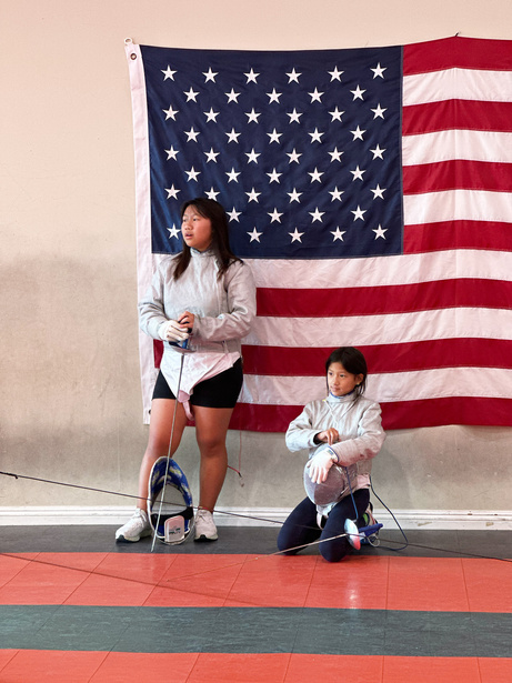 two individuals with fencing equipment in front of an american flag