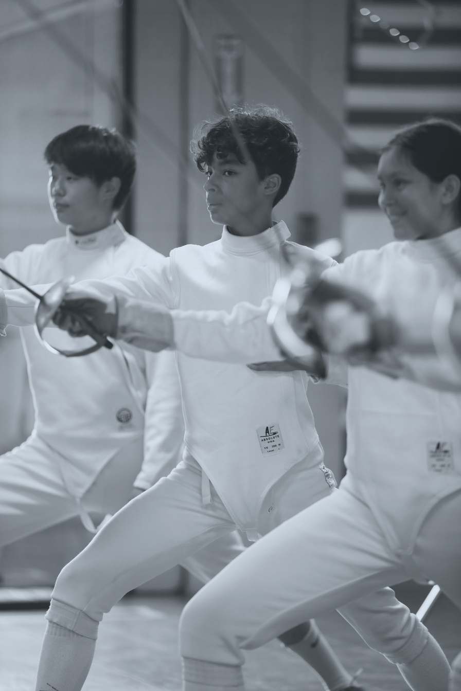a group of teenage people in fencing gear in en garde position with sabers in hand
